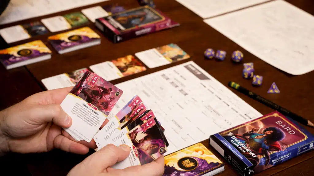 Person holding trading cards with game materials on a table